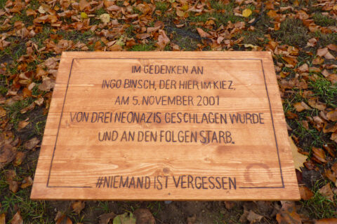 Das Foto zeigt eine hölzerne Gedentafel. Auf dieser steht: Im Gedenken an Ingo Binsch, der hier im Kiez am 5. November 2001 von drei Neonazis geschlagen wurde und an den Folgen starb. #niemandistvergessen
